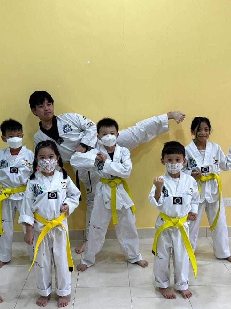 Children in taekwondo uniforms with yellow belts and their coach